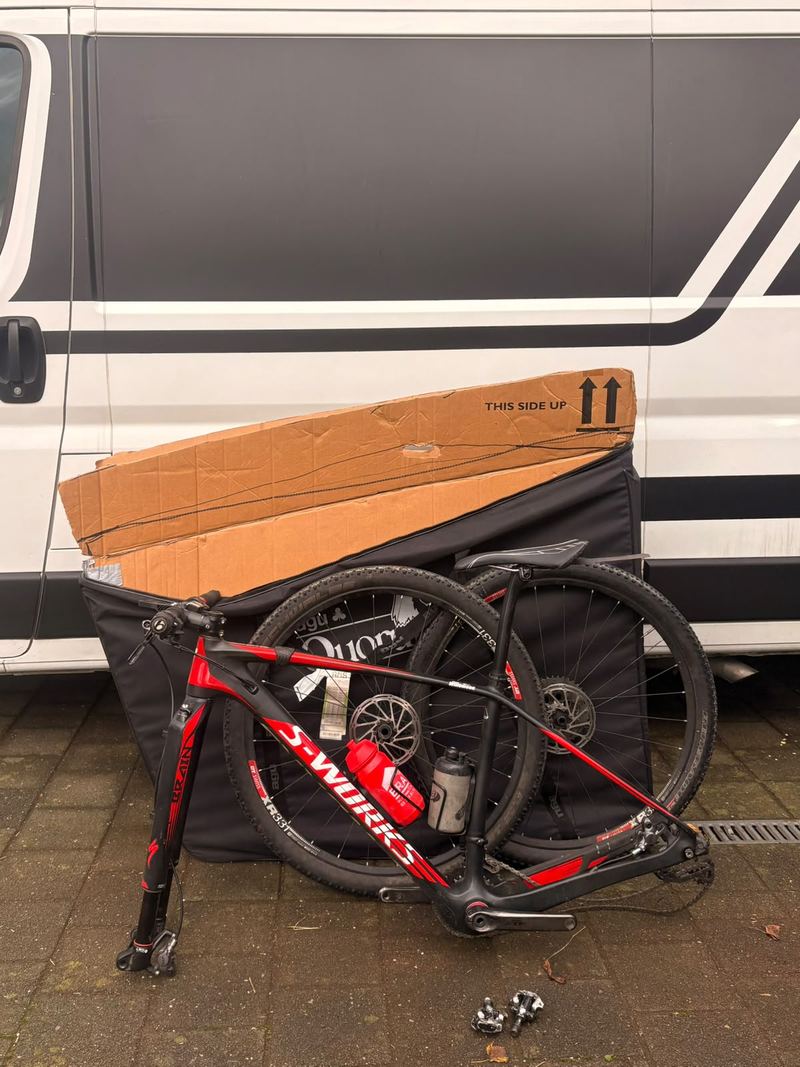 Mountainbike met losgemaakt voorwiel naast de fietstas en de kartonnen doos